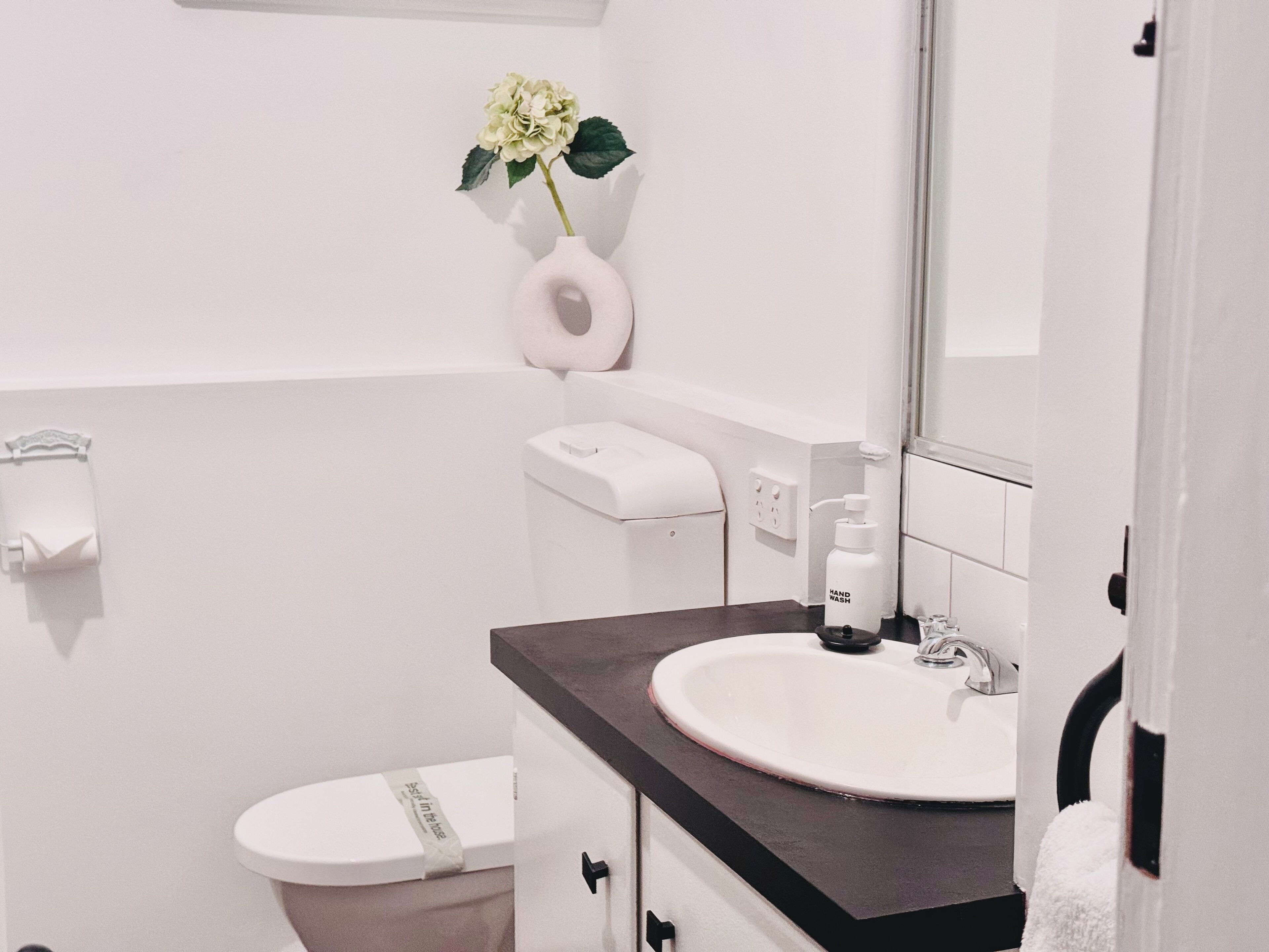 Un bagno moderno con un water bianco, un lavabo con piano d'appoggio scuro, un dispenser per sapone e un porta carta igienica.