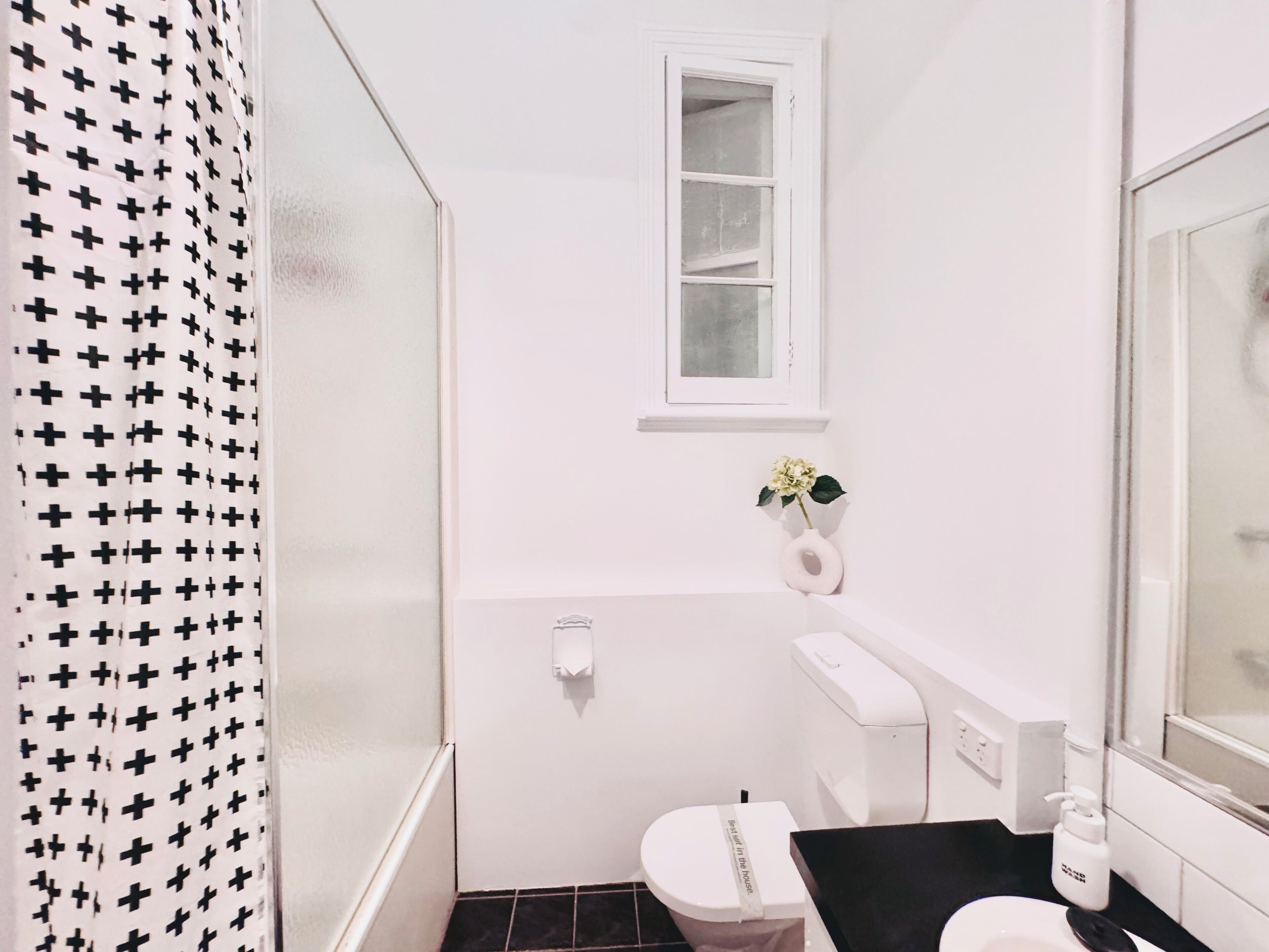 A small, white bathroom with a shower curtain, a toilet, a sink, and a window.