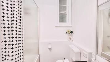 A small, white bathroom with a shower curtain, a toilet, a sink, and a window.