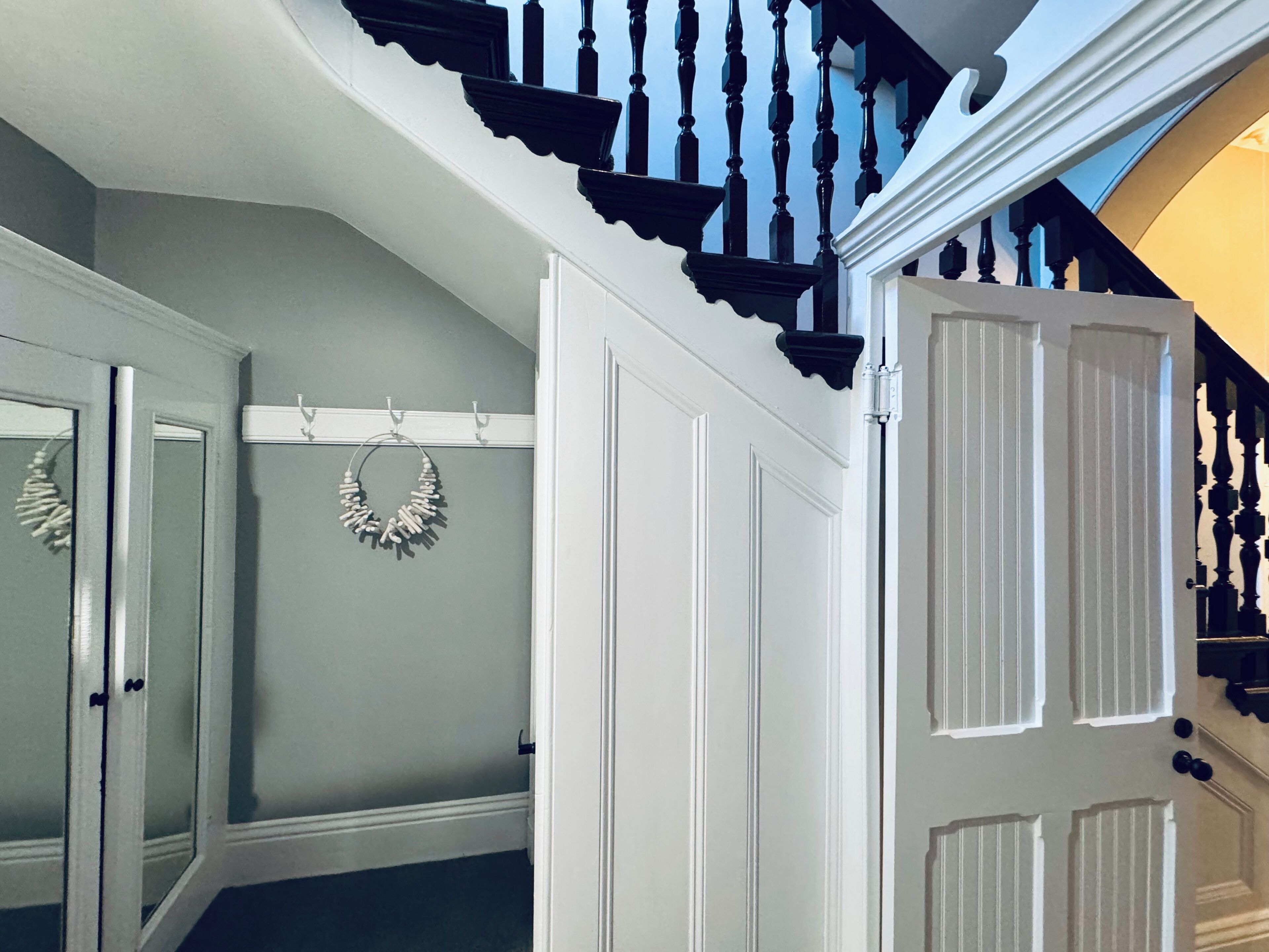 Eine Treppe mit schwarzen Spindeln und weißem Zierleisten, die zu einer Empore mit einer weißen Tür und einem an der Wand befestigten Kranz führt.