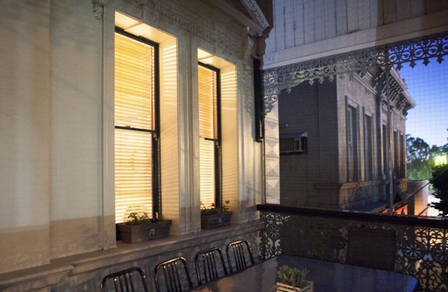 A balcony with a table and chairs, overlooking a building with large windows and ornate railings.