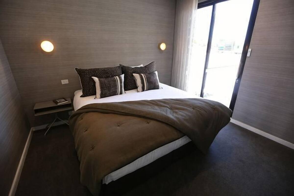 Una habitación de hotel con cama, mesita de noche y ventana.