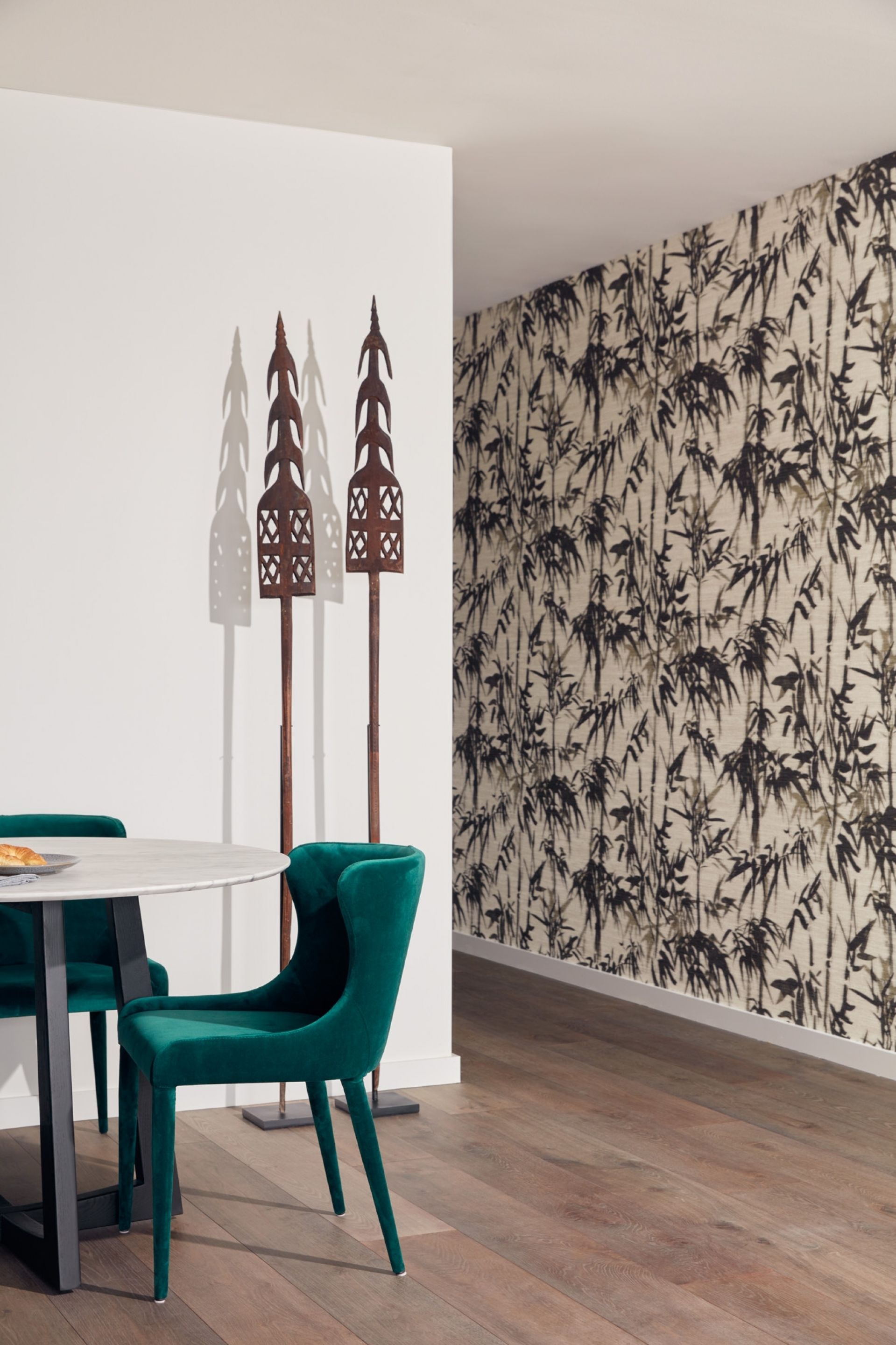 A dining area with a round table, teal chairs, and a wall with a bamboo pattern.