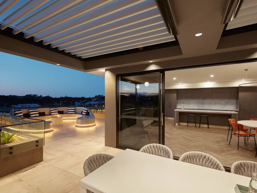 An outdoor dining area with a glass wall, a kitchen with a marble countertop, and a seating area with a fire feature.