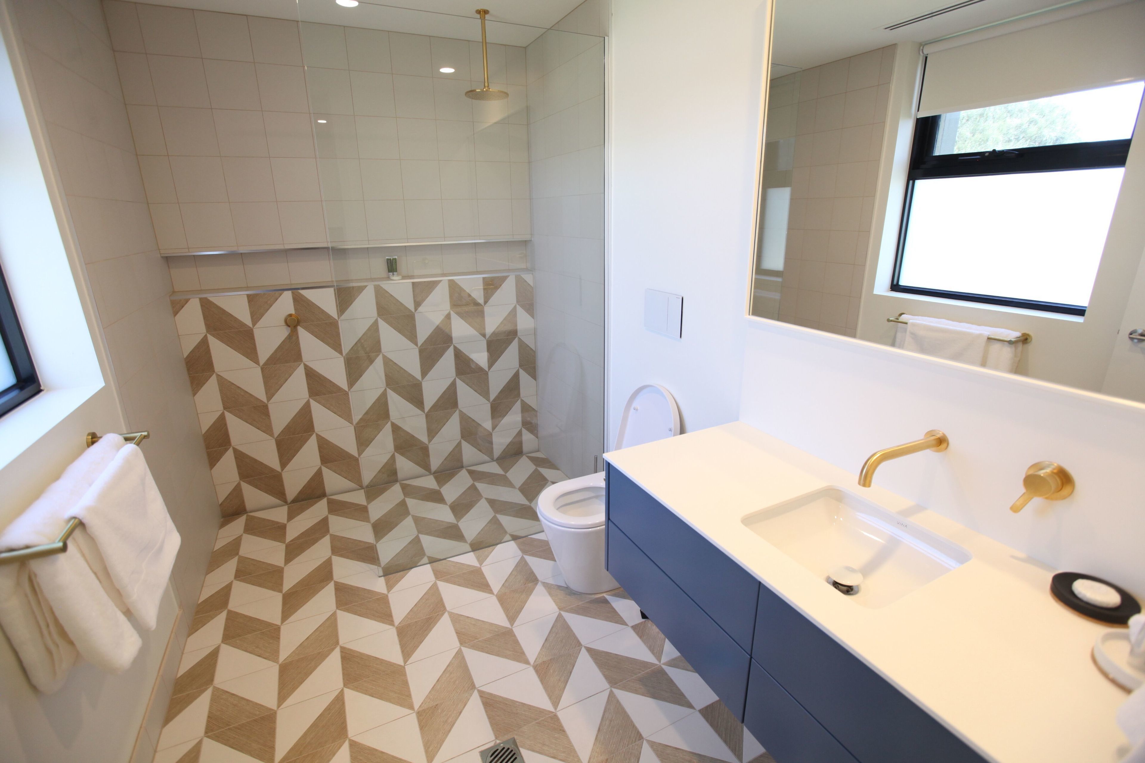 A modern bathroom with a geometric patterned floor, a dual sink vanity, and a shower area.