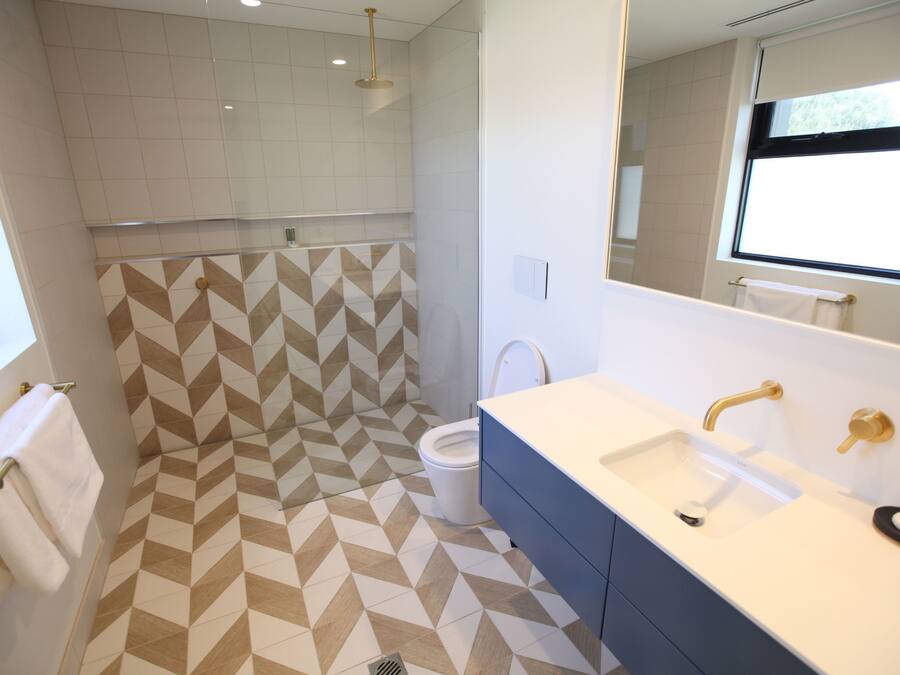 A modern bathroom with a geometric patterned floor, a dual sink vanity, and a shower area.