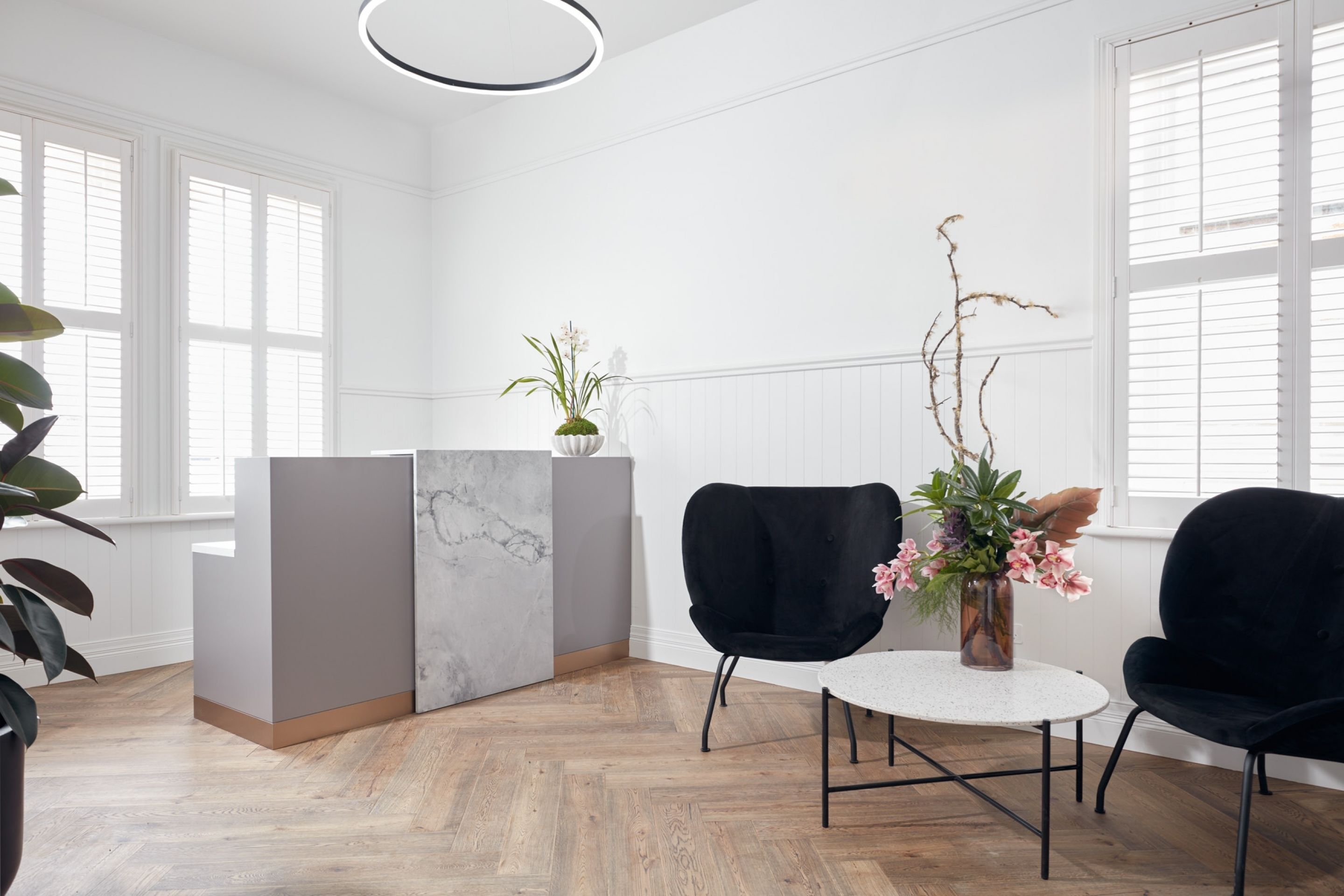 A modern reception area with a marble counter, two black chairs, and a vase with flowers.