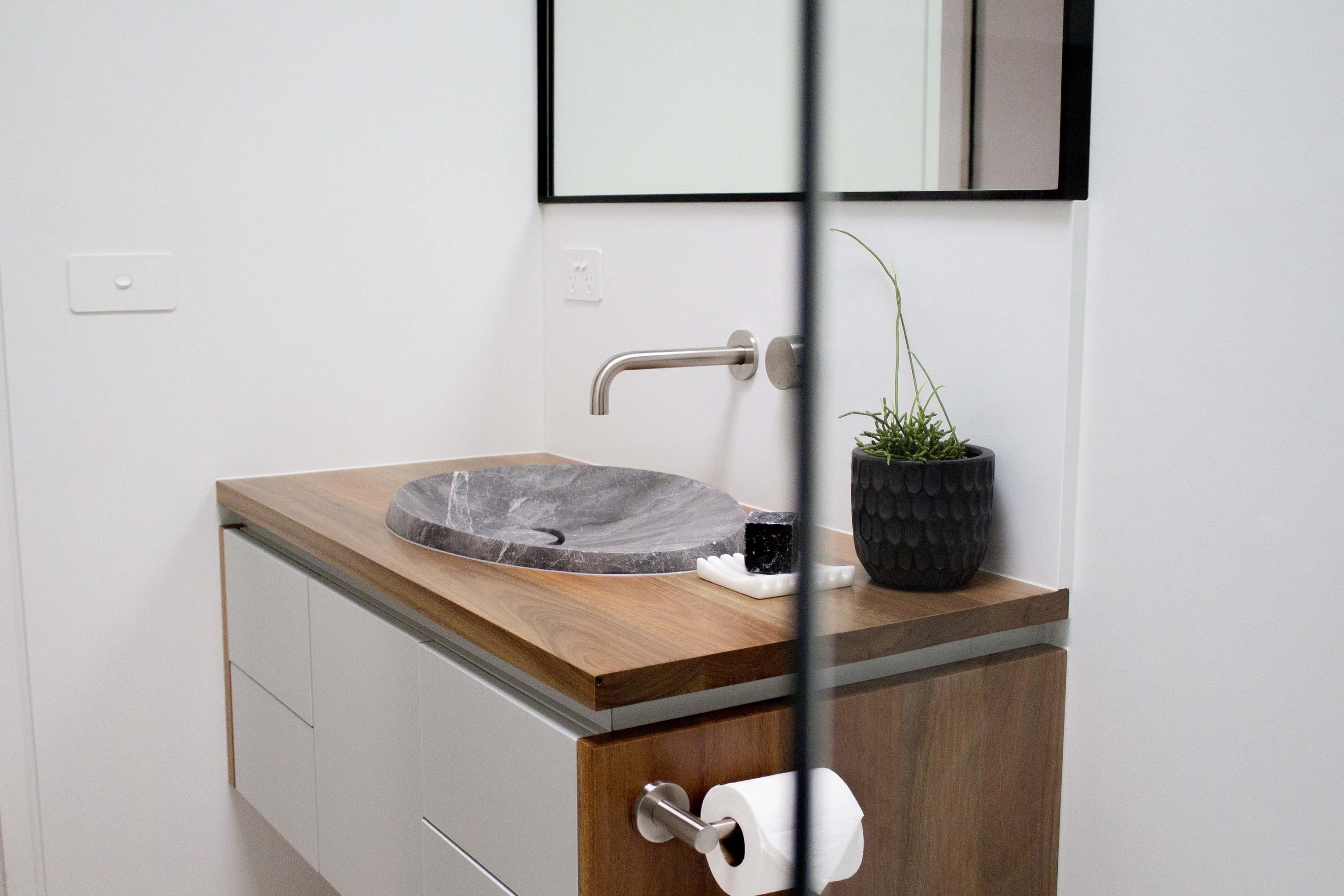 Un baño con tocador de madera, lavamanos de piedra, espejo y planta en maceta.