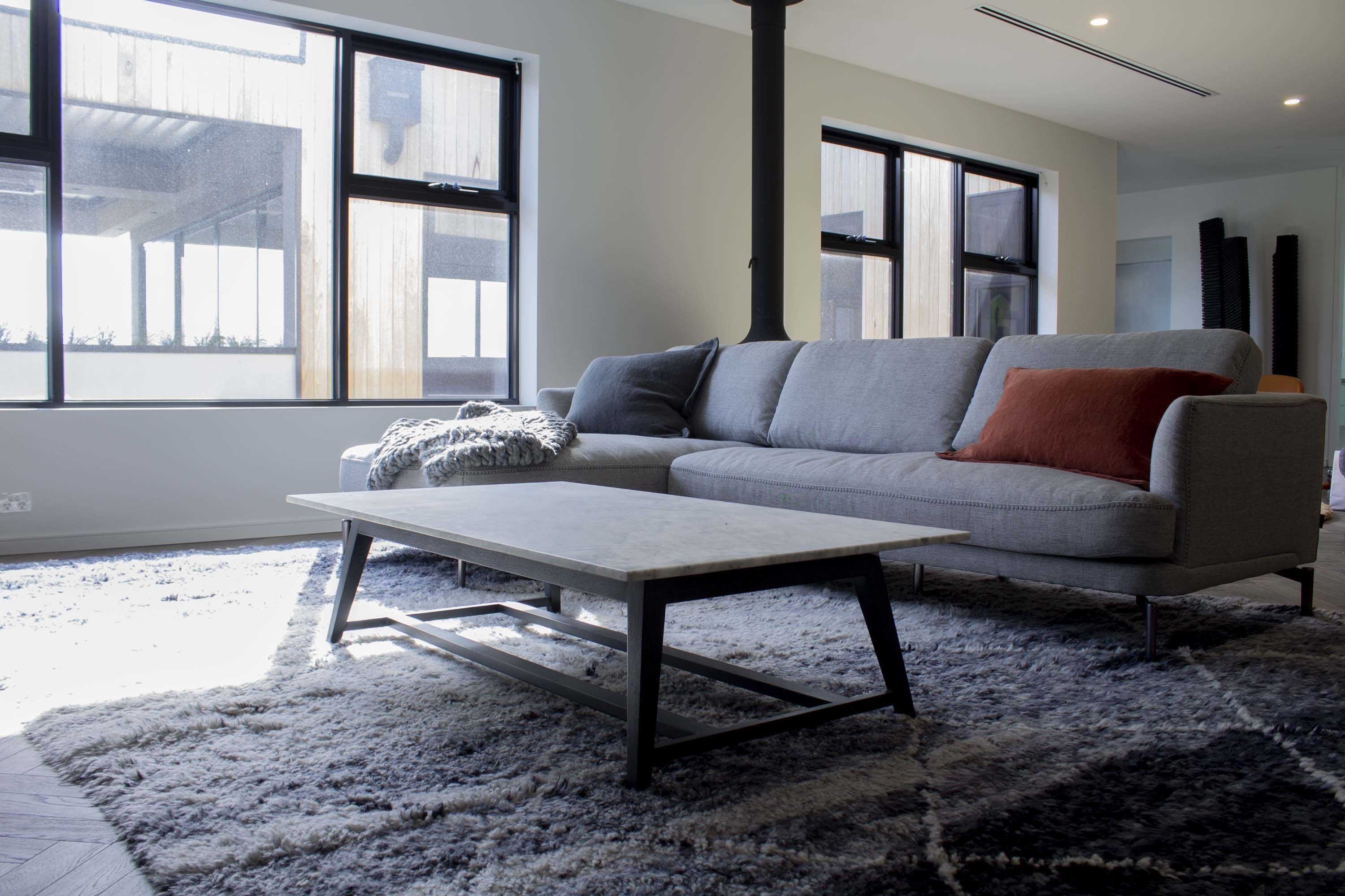 Una sala de estar moderna con un sofá gris, una mesa de centro blanca y un ventanal que proporciona luz natural.