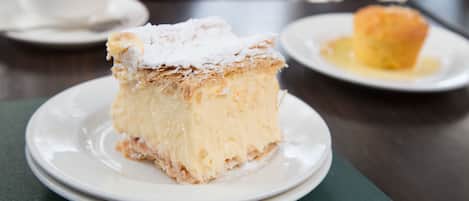 Une part de gâteau sur une assiette, saupoudrée de sucre glace, un muffin nappé de sirop et une tasse de café posée sur une soucoupe.