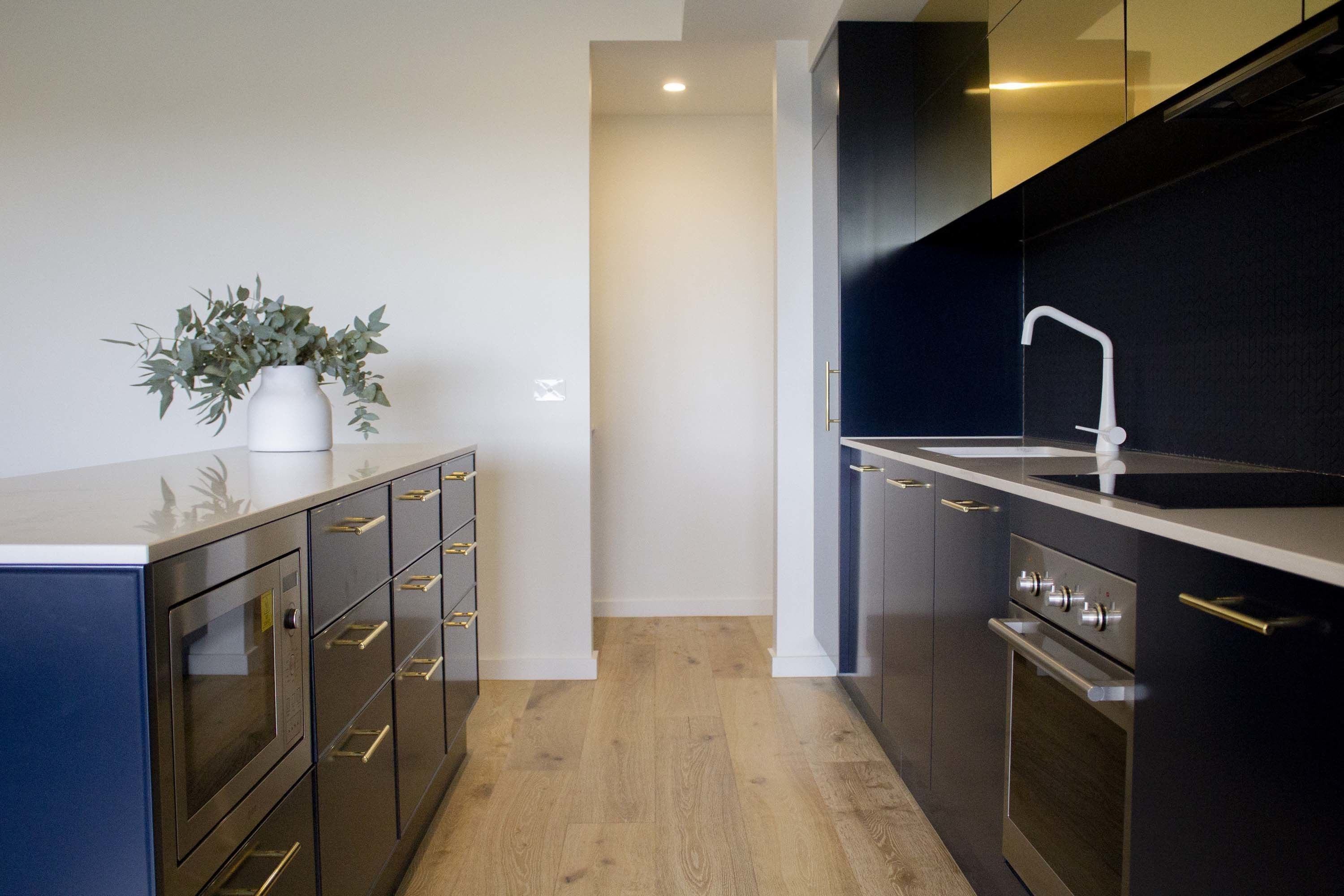 A modern kitchen with dark cabinetry, stainless steel appliances, and a white countertop.