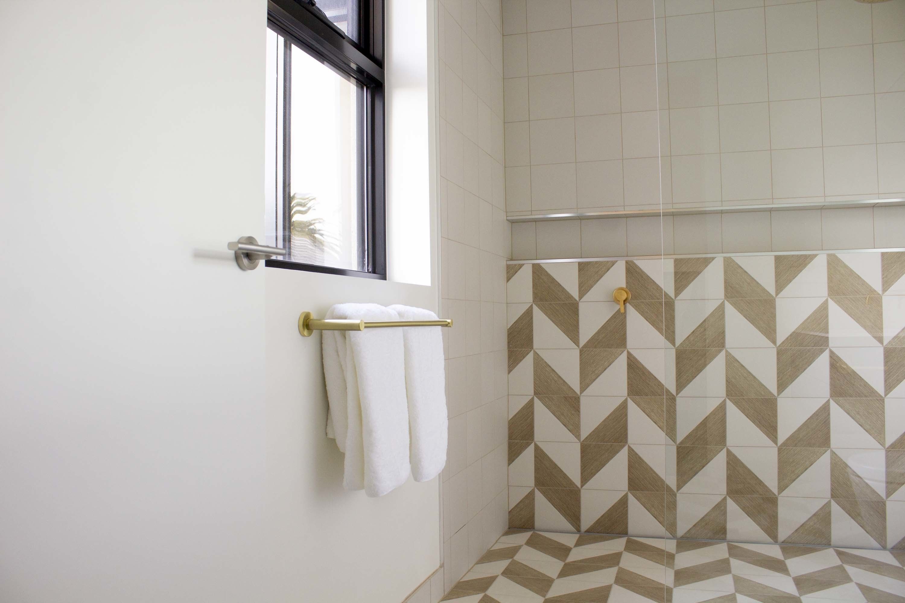 A bathroom with a geometric patterned tile wall, a window with a towel rack, and a door.