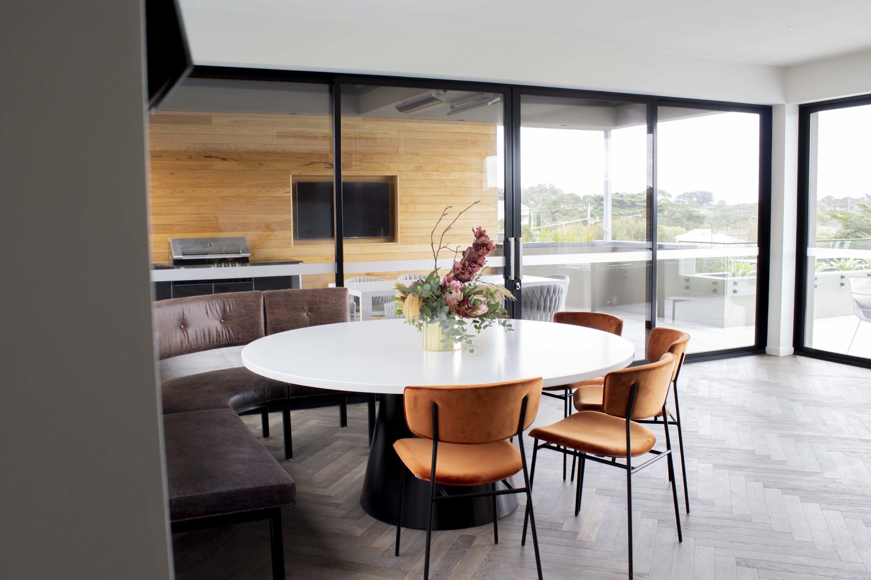A modern dining area with a round table, leather seating, and a large window offering a view of the outdoors.
