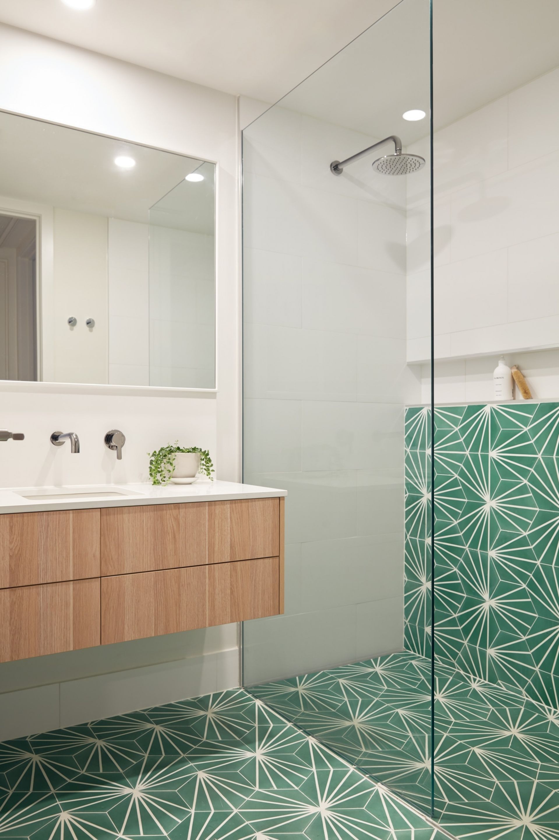 A modern bathroom with a large mirror, wooden vanity, and a shower with geometric-patterned tiles.