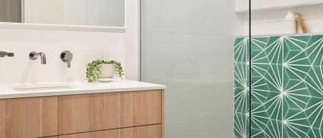 A modern bathroom with a large mirror, wooden vanity, and a shower with geometric-patterned tiles.