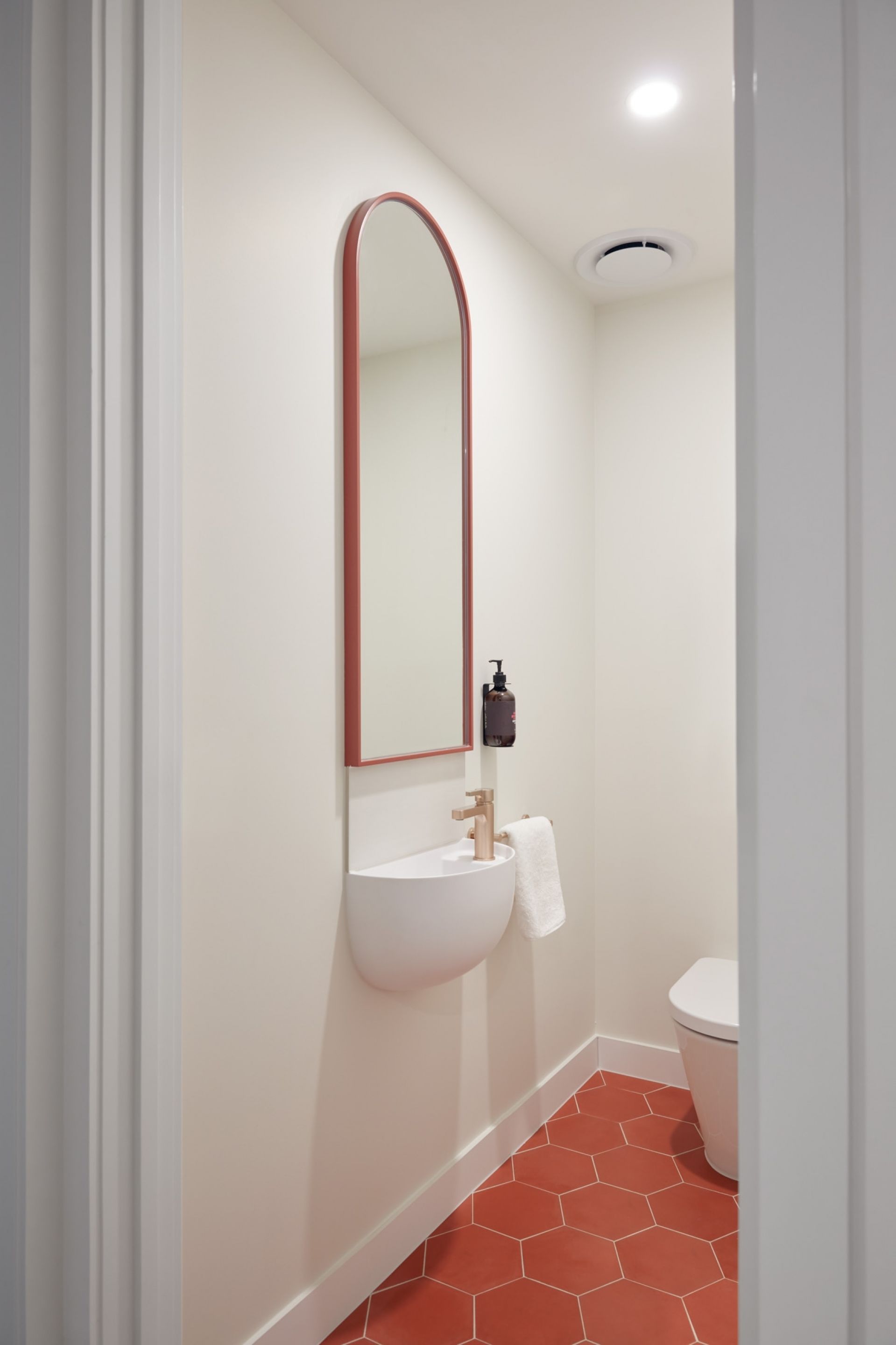A bathroom with a white sink, a mirror with a red frame, a white toilet, and a red-tiled floor.