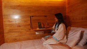 A wooden cabin room with a bed, a laptop on a shelf, and a small table with a flower. - Dbeds Hostel By Soscomma (Kuta)