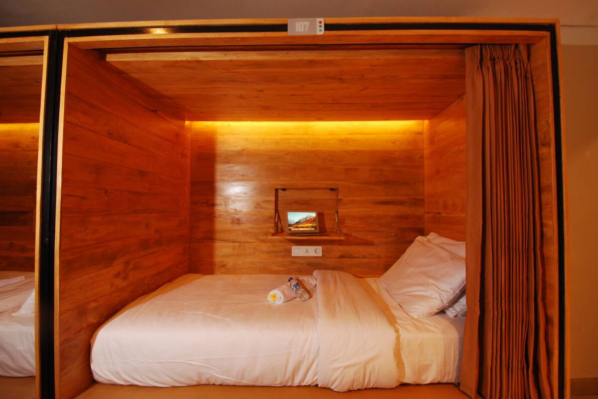 A wooden cabin-style room with a single bed, a small shelf with a television, and a curtain.
