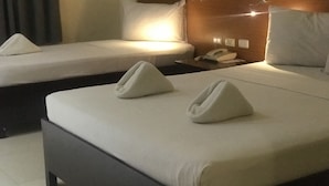 Ein Hotelzimmer mit zwei Einzelbetten, jeweils mit Kissen und einem Handtuch. Ein Nachttisch mit Telefon und Lampe ist vorhanden.