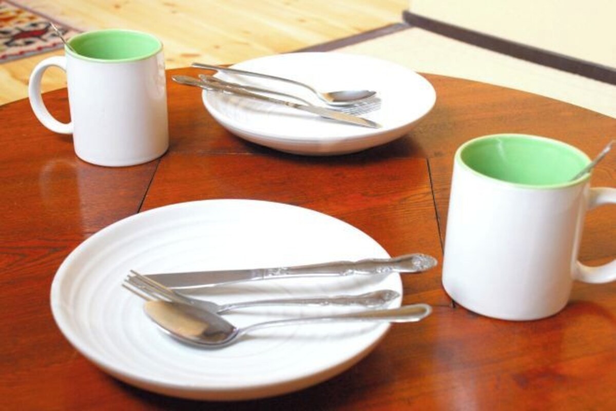 A round wooden table with three white plates, each with a spoon and fork, and a white mug with a green interior.