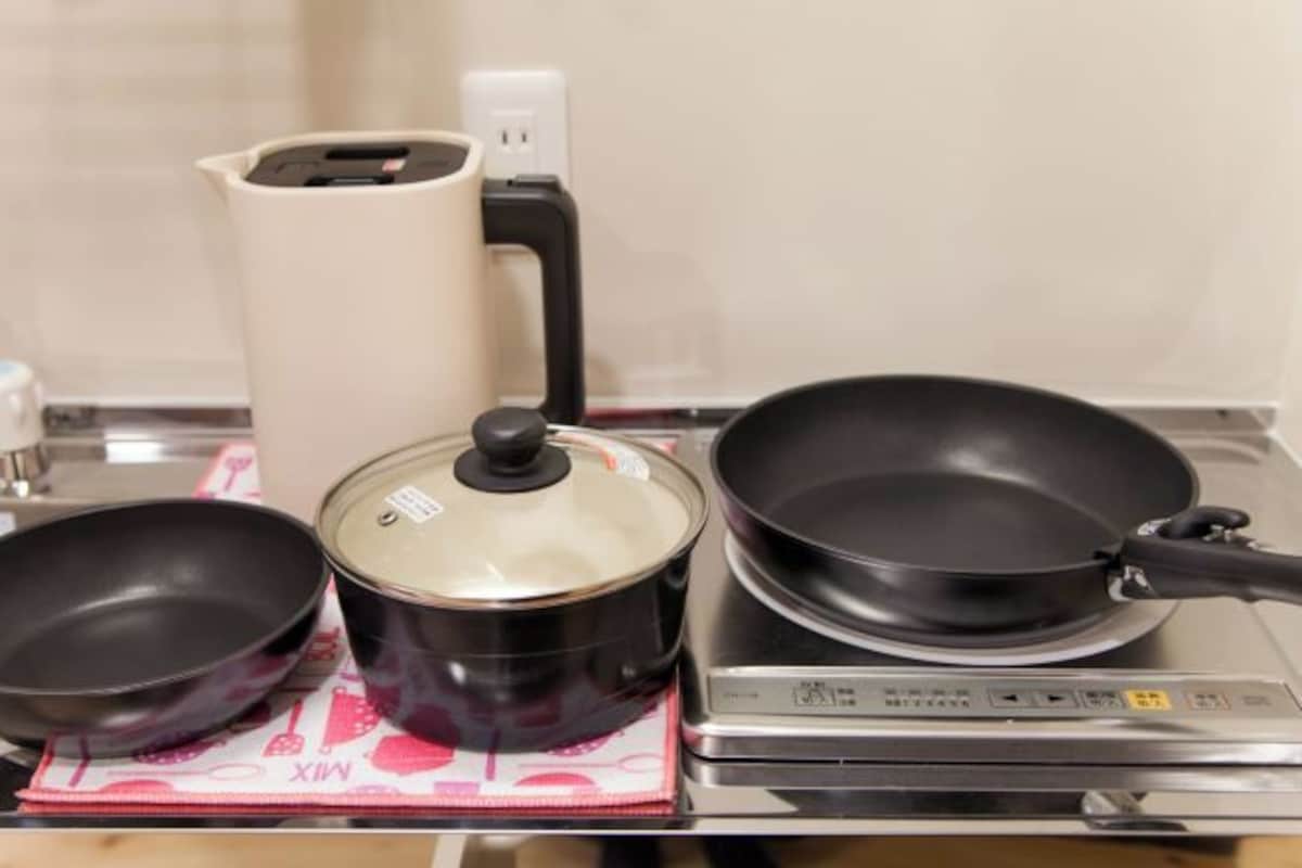 Una cocina con estufa, sartén, olla y tetera.