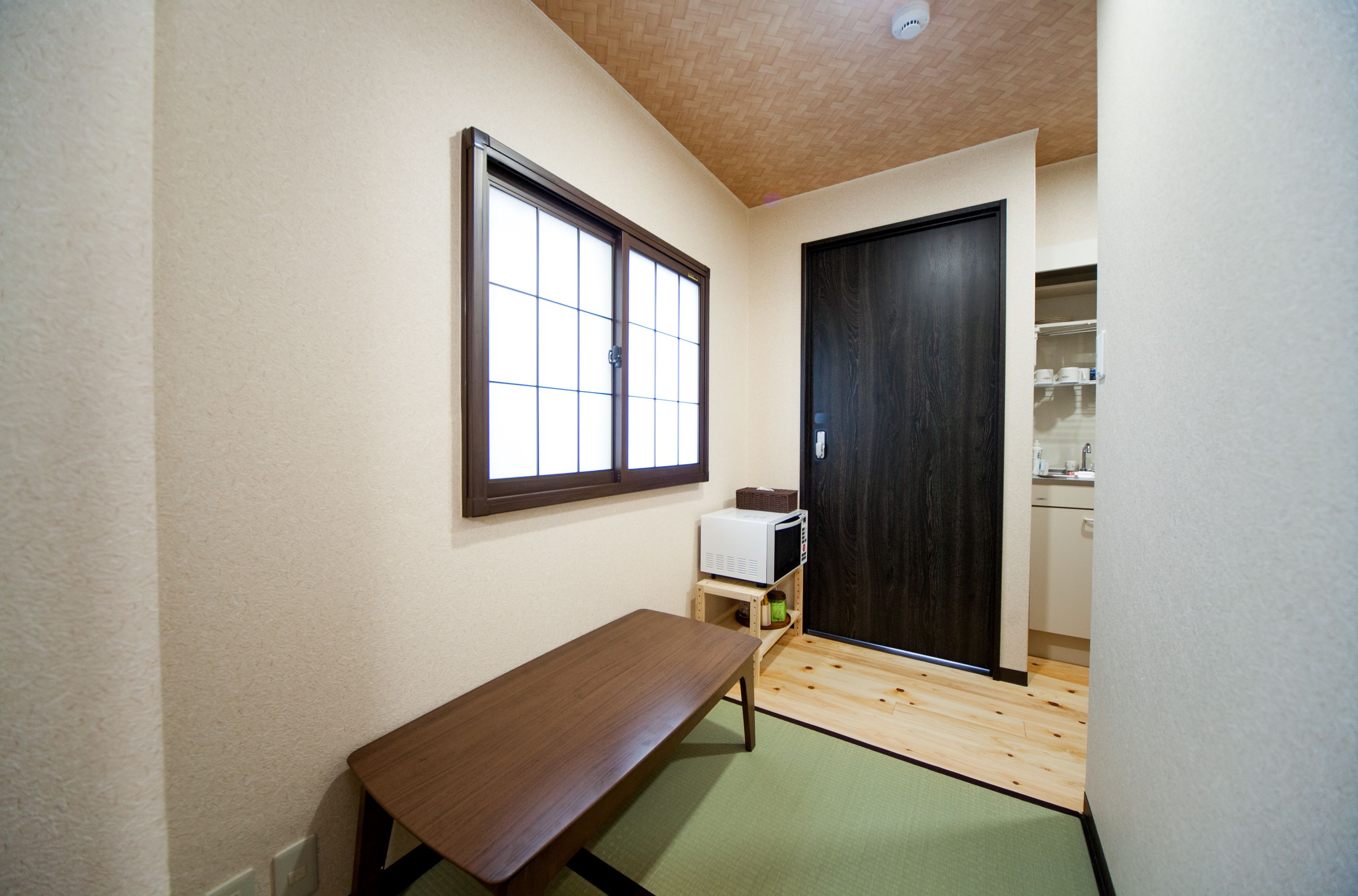 A small room with a wooden bench, a microwave on a shelf, and a sliding door leading to a kitchen area.