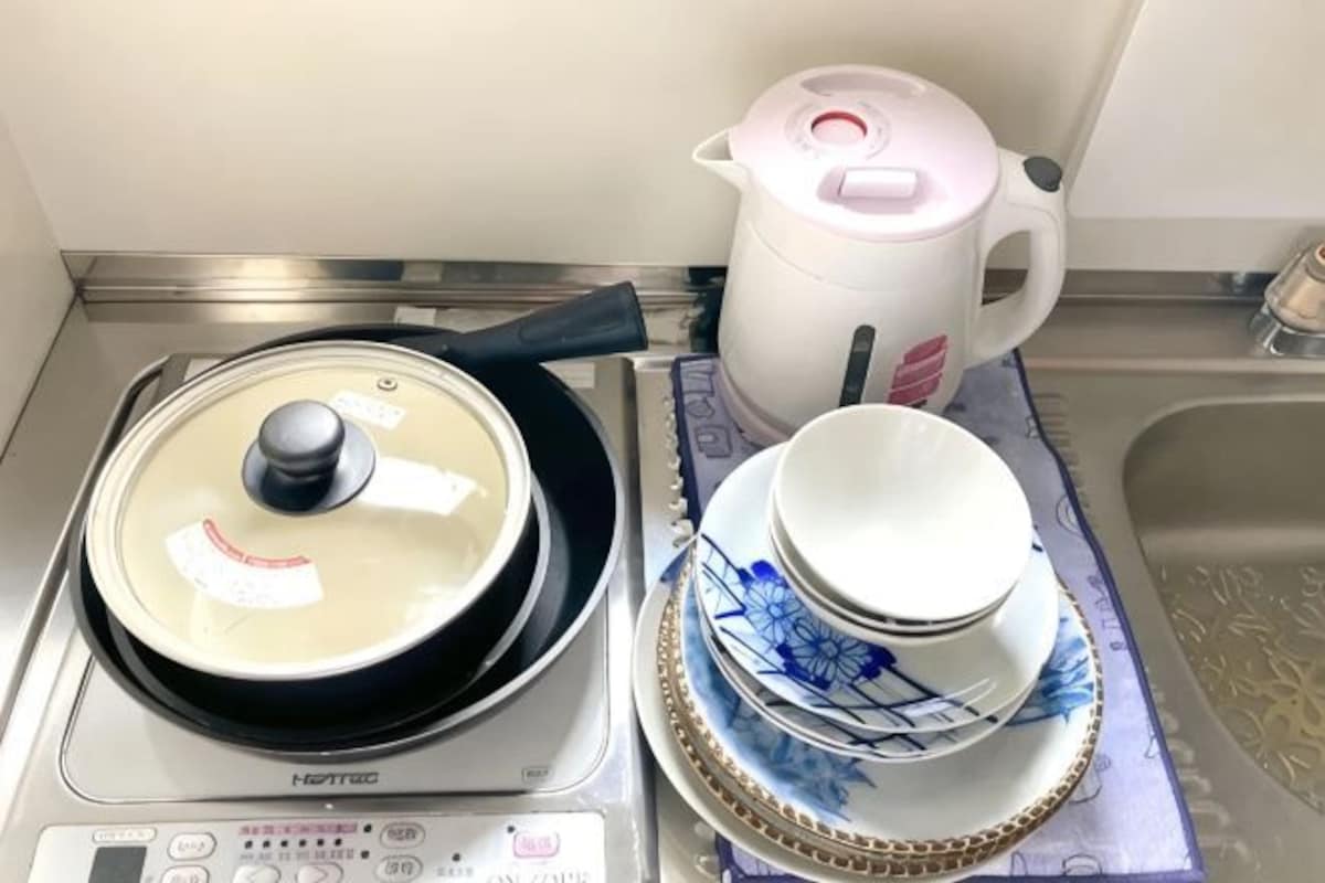 Una cocina con estufa, hervidor y platos apilados.