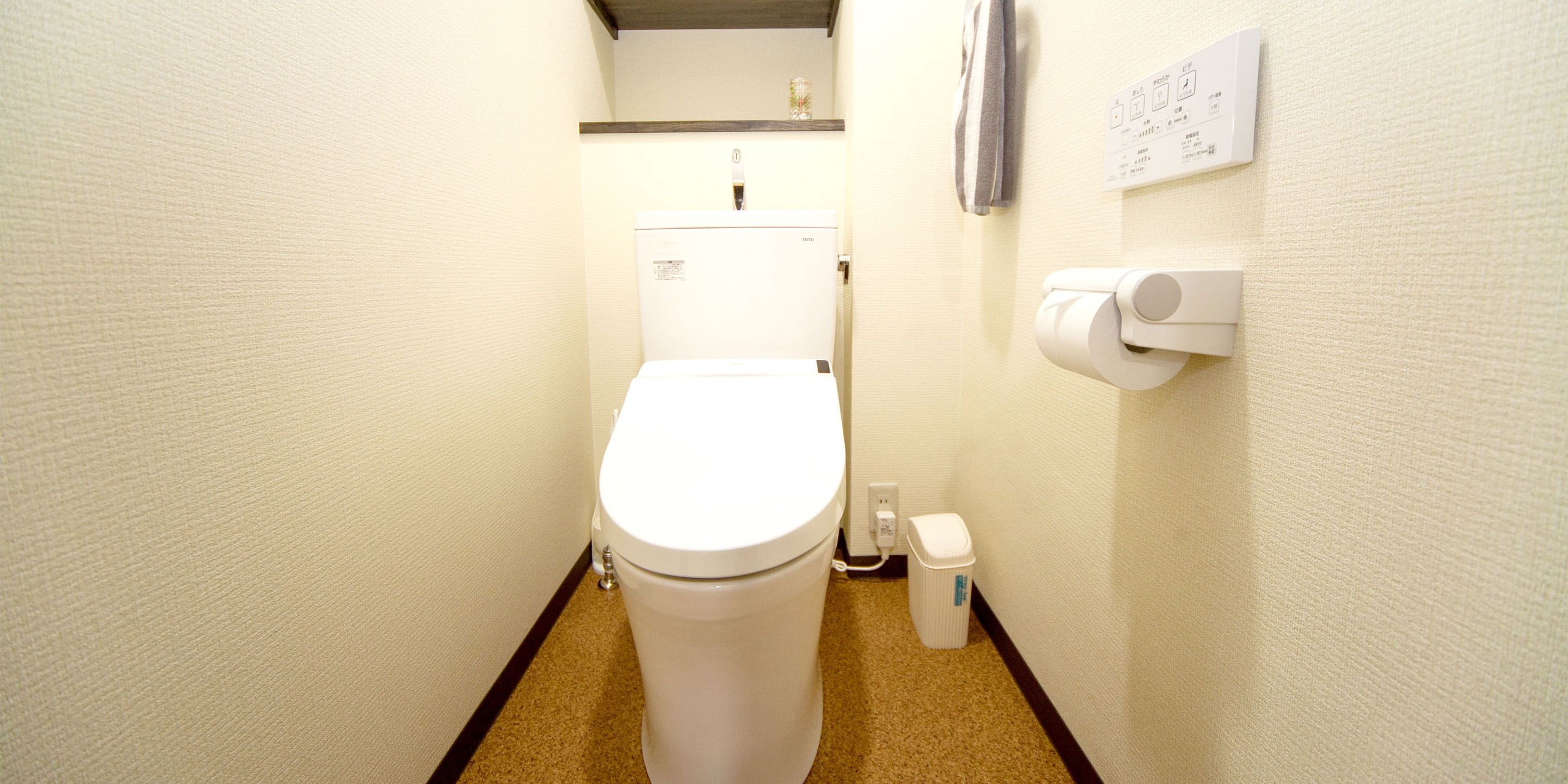 A small, clean bathroom with a toilet, a trash can, and a paper towel dispenser.