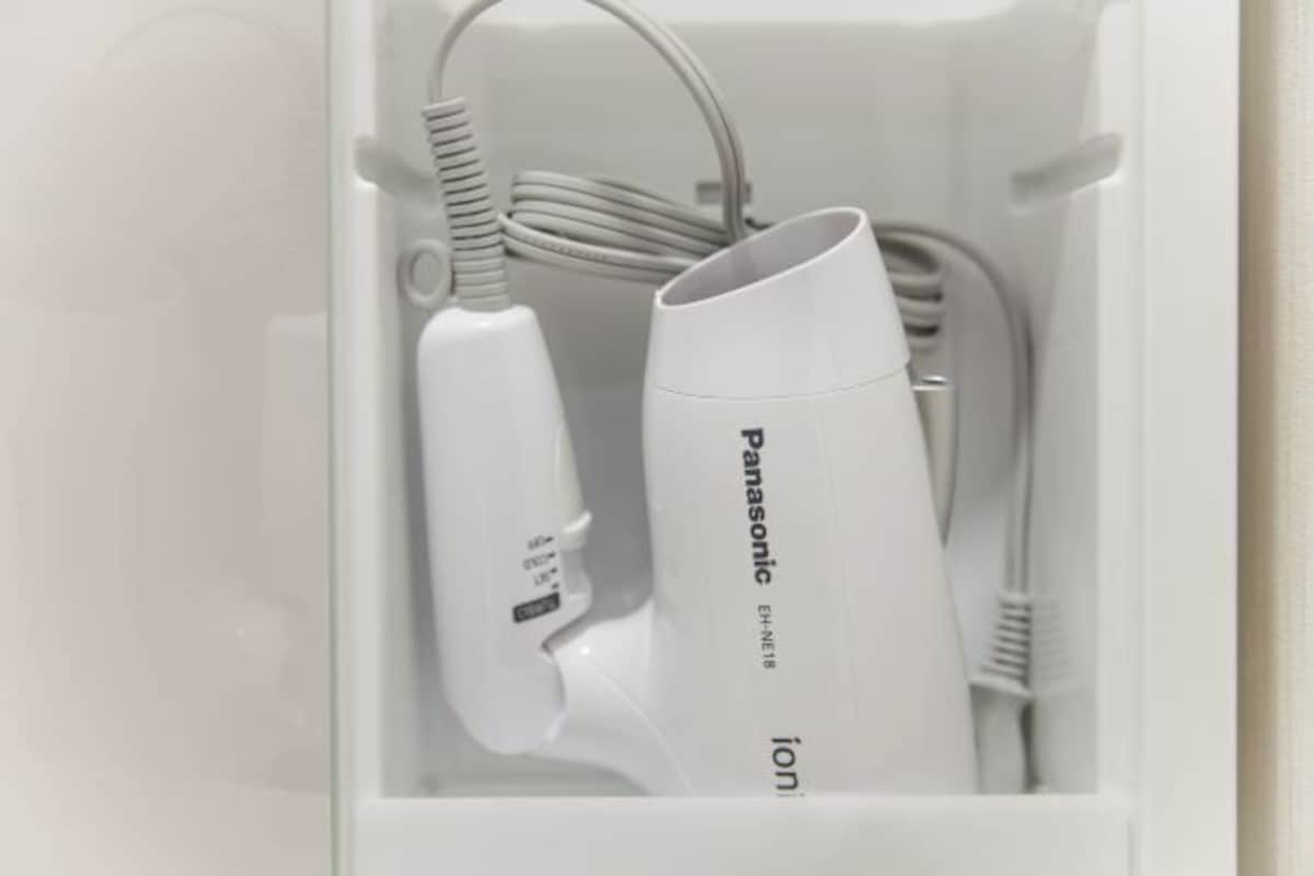 Un cajón blanco que contiene un secador de pelo iónico Panasonic y un cable de carga blanco.