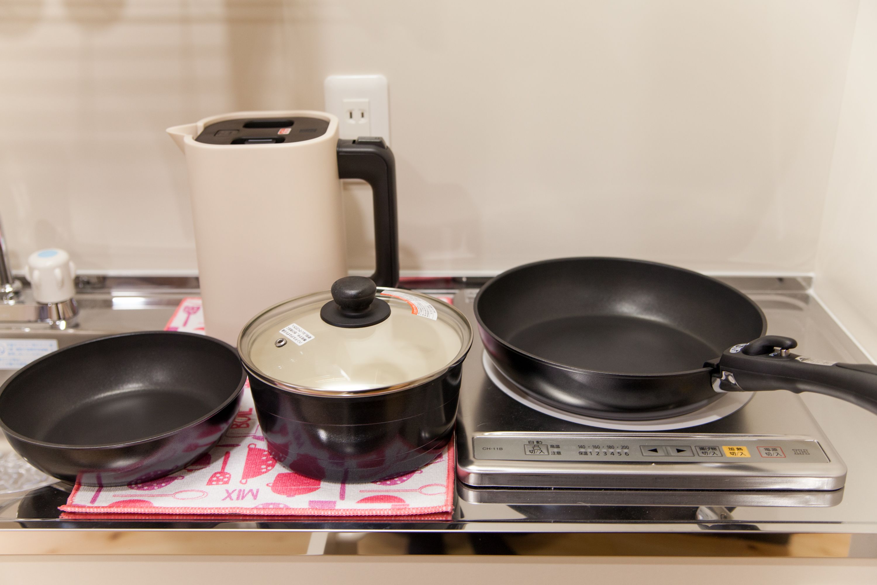 A kitchen with a stove, a pot, a pan, and a kettle.