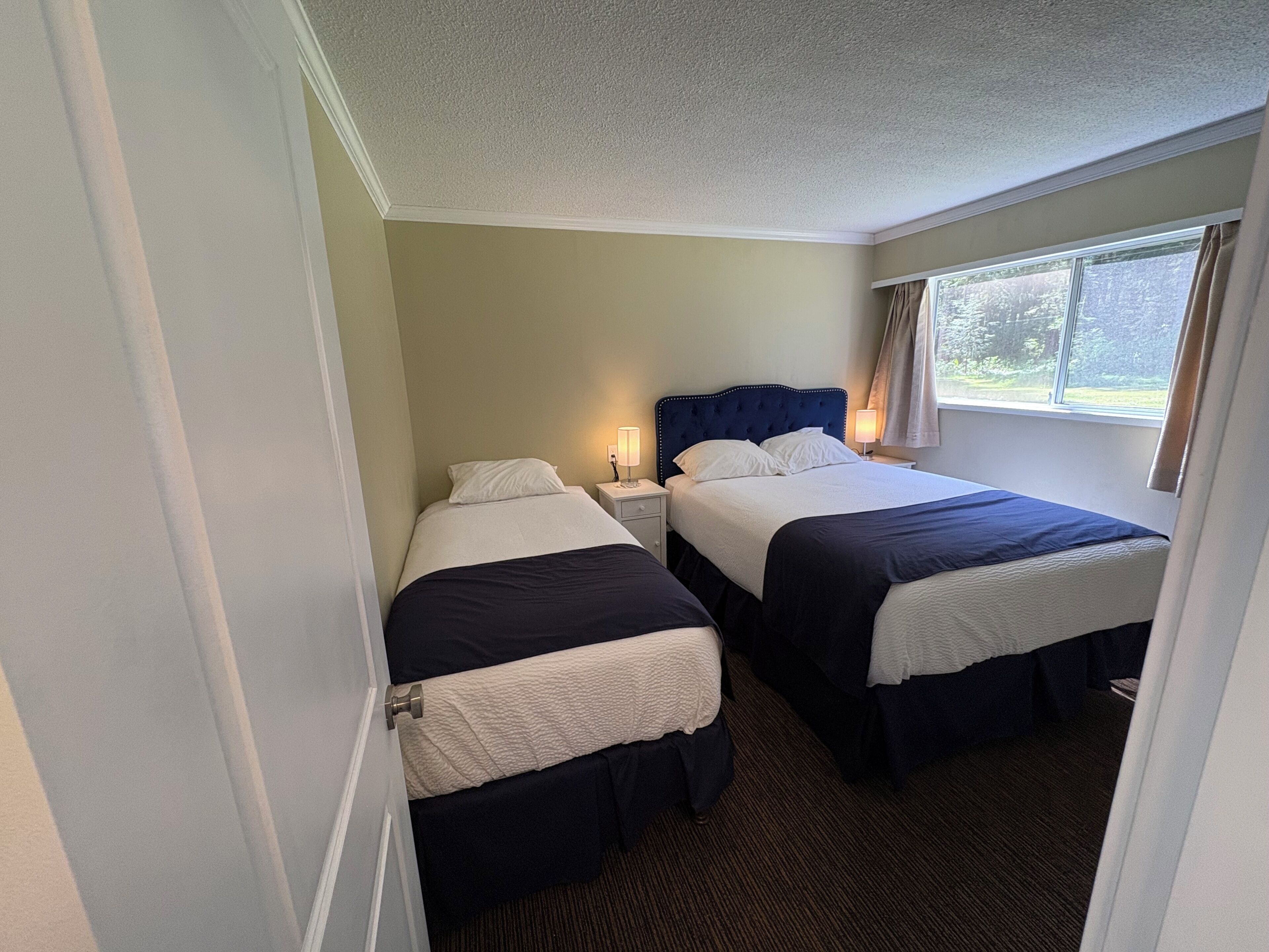 A hotel room with two beds, a window with curtains, and a door.