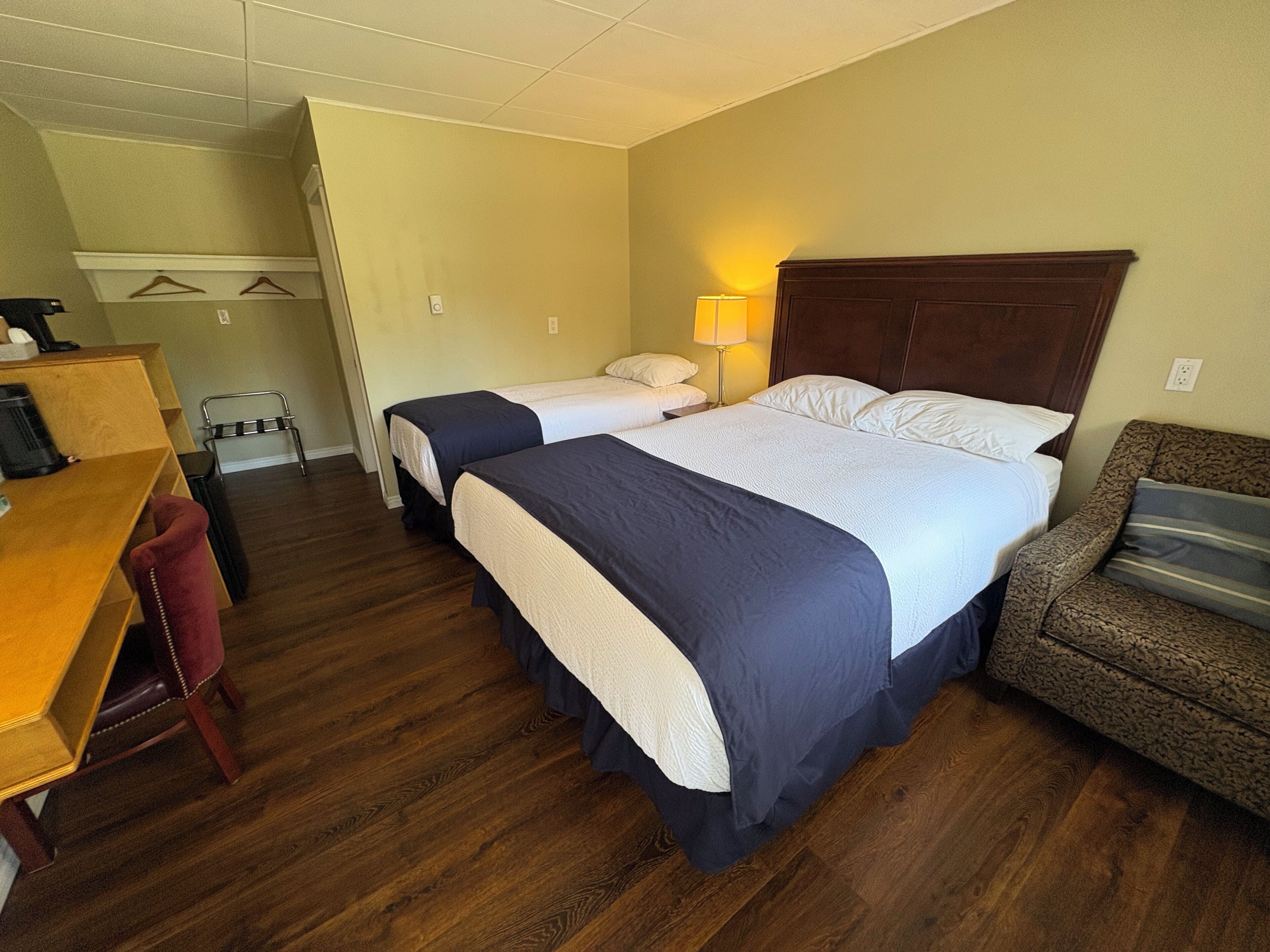 A hotel room with two beds, a desk, a chair, a lamp, and a couch.
