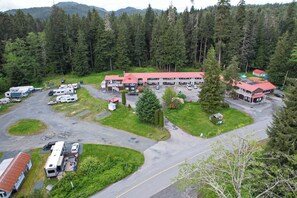Um camping com veículos recreativos, um edifício grande com telhado vermelho e uma montanha arborizada ao fundo.