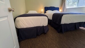 Ein Hotelzimmer mit zwei Betten, einer Tür, einem Fenster und einem Teppichboden.