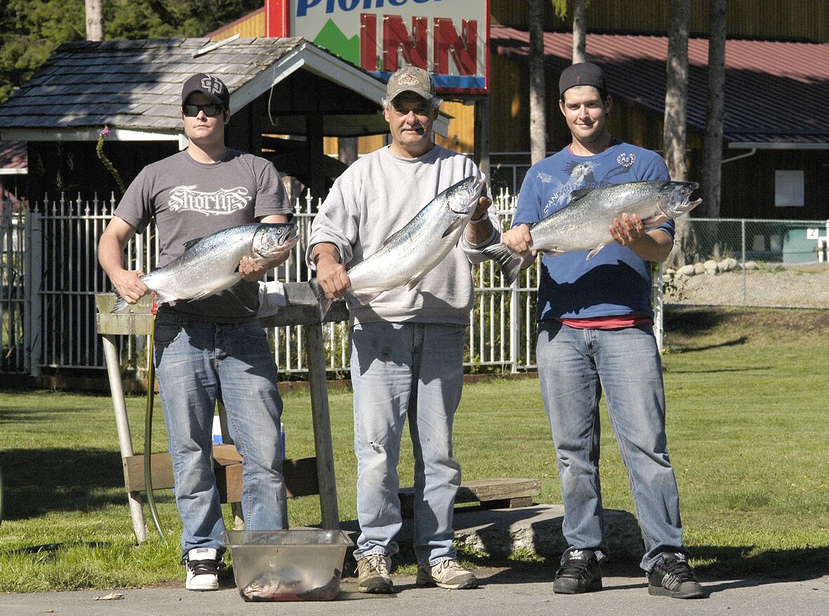 Três pessoas segurando peixes grandes em frente a um edifício com uma placa que diz "Pioneer Inn".