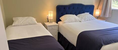 Two beds with white linens, a blue headboard, bedside lamps, and a nightstand with a lamp.