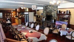 Ein Restaurant mit mehreren Tischen und Stühlen, einem Kamin aus Stein und einer Küche im Hintergrund.
