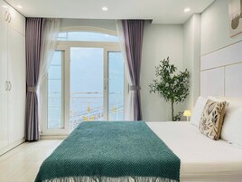 A bedroom with a bed, curtains, a plant, and a view through a window.