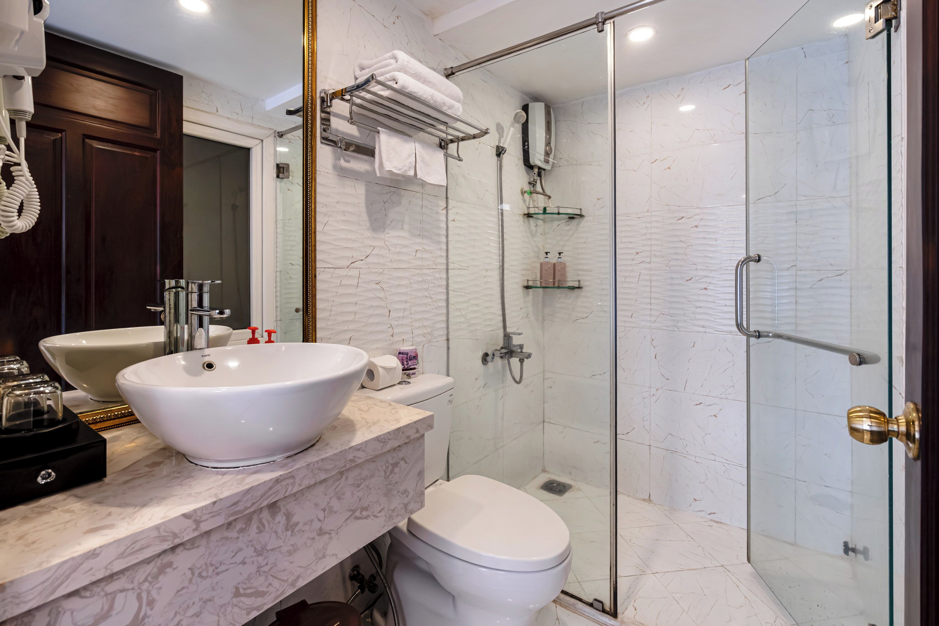 Een badkamer met een grote witte wastafel, een toilet, een douchecabine van glas en een handdoekrek met opgevouwen handdoeken.