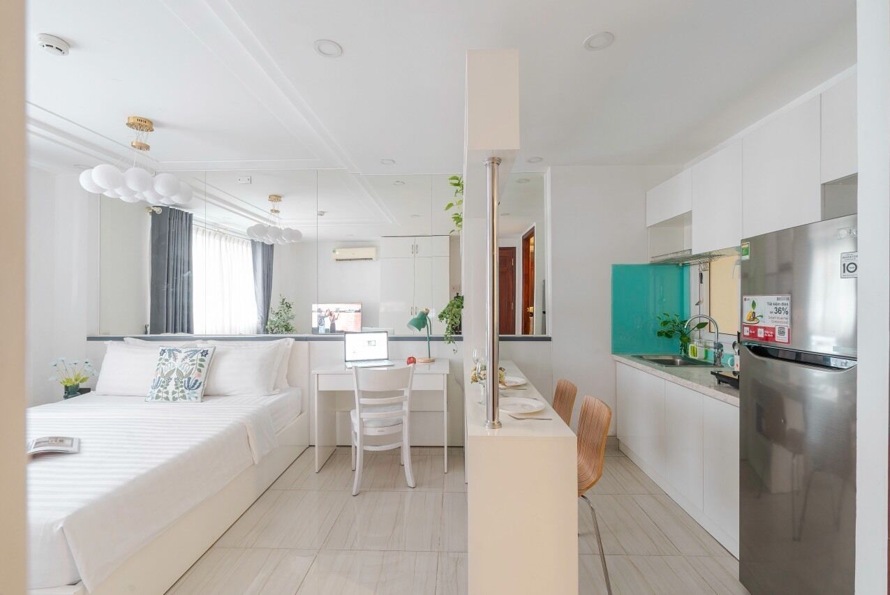 A modern hotel room with a bed, a desk, a chair, a kitchenette, and a bathroom.