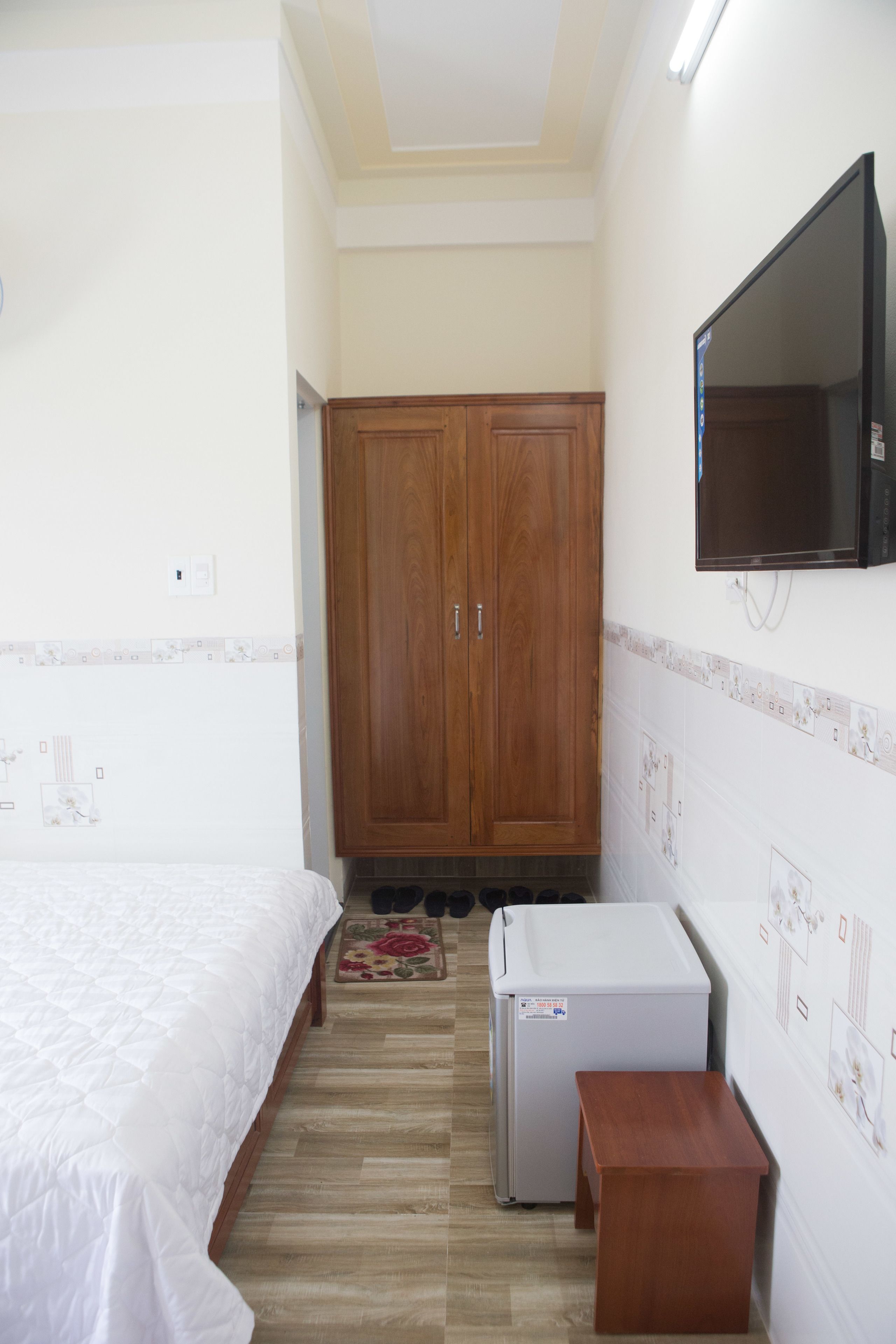 Un dormitorio con cama, armario de madera, una mesita y televisor montado en la pared.
