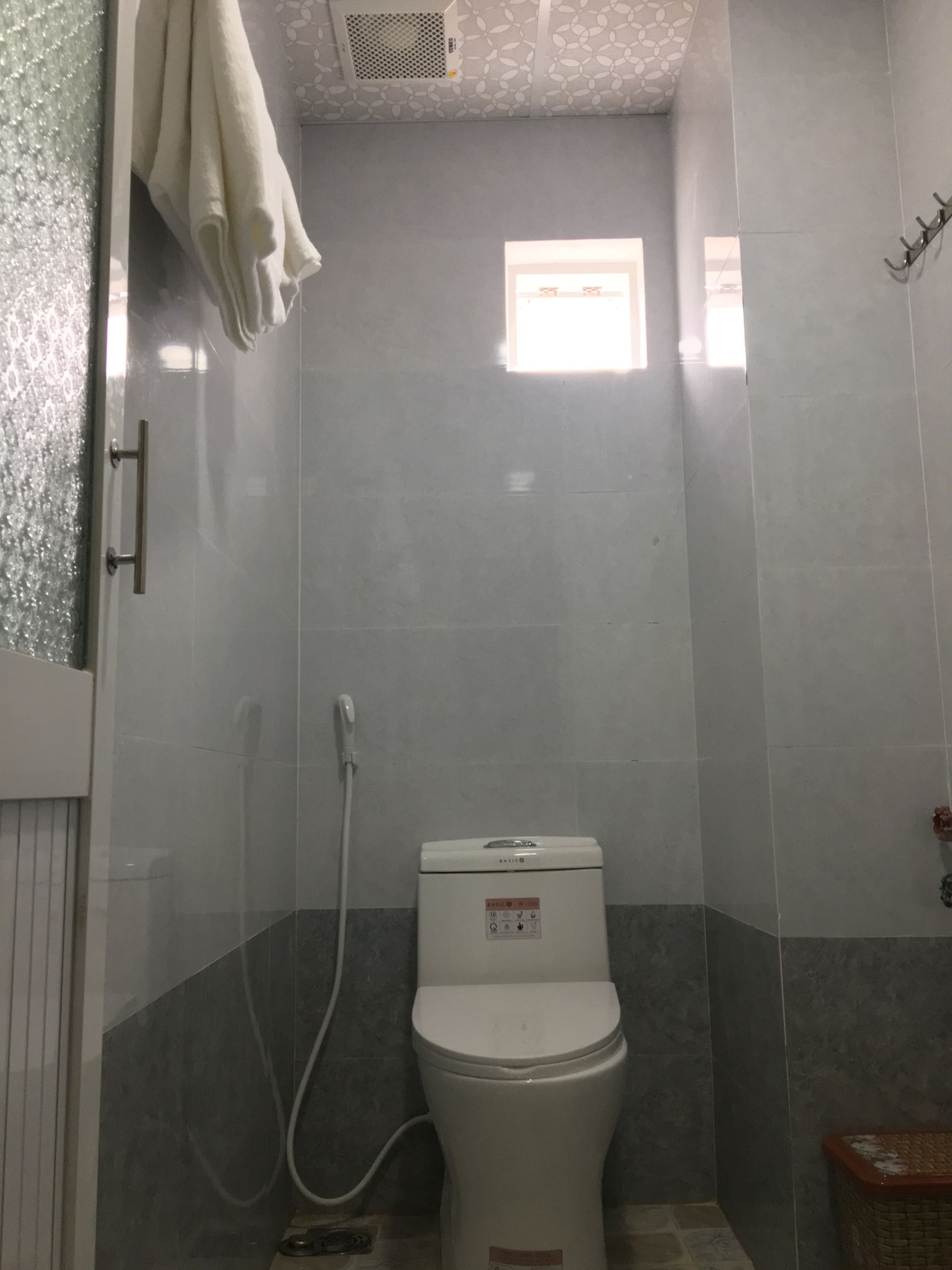 A small, enclosed shower stall with a toilet, a towel rack, and a small window.