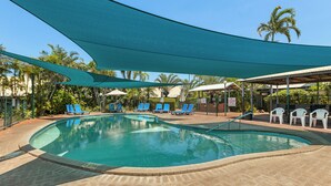 Una piscina con sillones azules para tomar el sol y una zona con sombra.