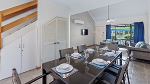 Comedor con una mesa larga dispuesta para seis personas, rodeado de mobiliario de mimbre.