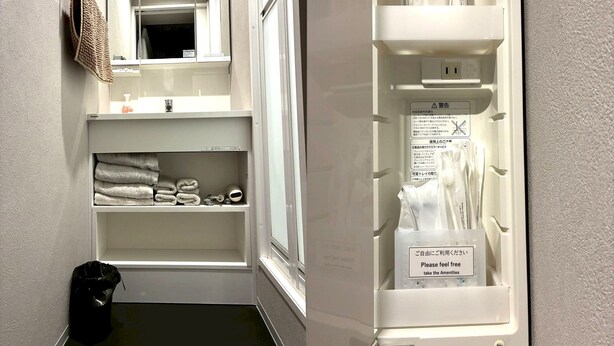 Une salle de bain d’hôtel équipée d’un miroir, d’un porte-serviettes, d’étagères avec des serviettes et d’autres articles de toilette, comme une brosse à cheveux et des mouchoirs.