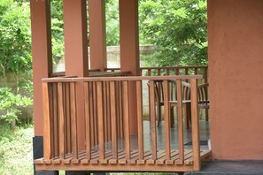 A wooden balcony with vertical railings and a view of greenery in the background. - The Bell Farm Eco Resort (Kandalama)