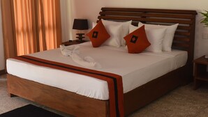 A neatly made bed with a wooden headboard, white bedding, and two red pillows with a black diamond pattern. - The Bell Farm Eco Resort (Kandalama)