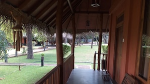 A covered porch with wooden railings, a bench, and a view of a well-maintained lawn and trees. - The Bell Farm Eco Resort (Kandalama)