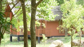 A thatched-roof building with a wooden deck, surrounded by trees and grass. - The Bell Farm Eco Resort (Kandalama)