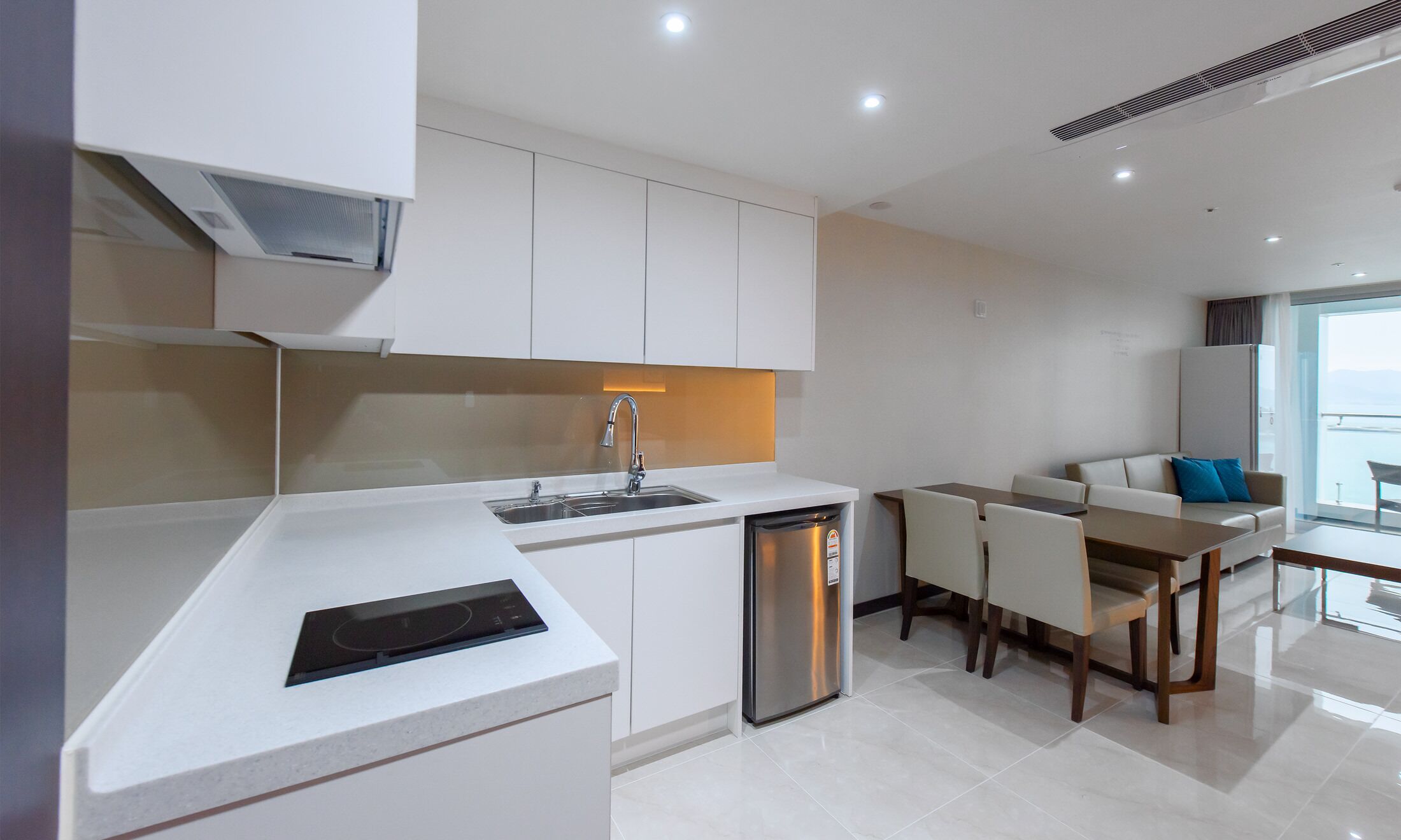 Una cocina moderna con armarios blancos, lavavajillas integrado y un comedor con mesa y sillas.